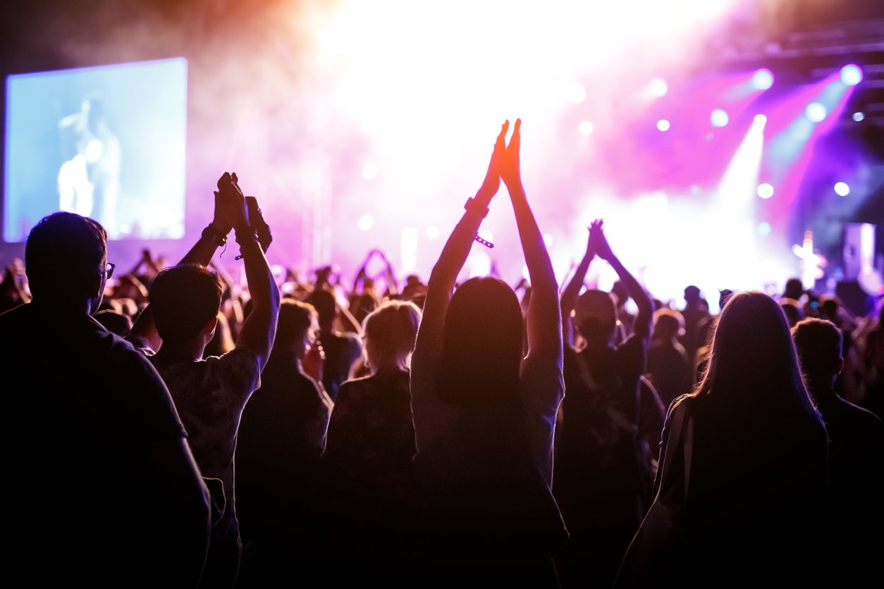 People with raised hands, silhouettes of bangkok concert crowd in front of bright stage light